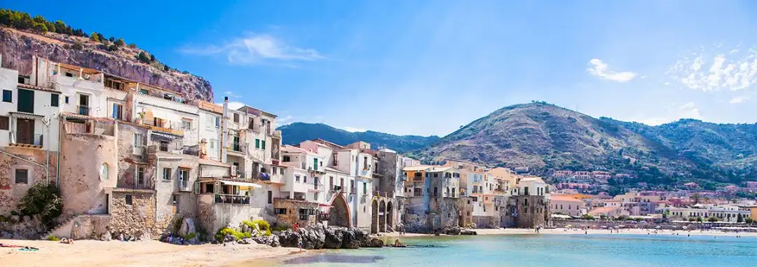 panorama di un paesino siciliano in riva al mare con una barchetta in primo piano