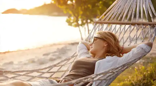 avslappnad kvinna kvinna på stranden som ligger i en hängmatta med solglasögon och tittar på havet helt avslappnad